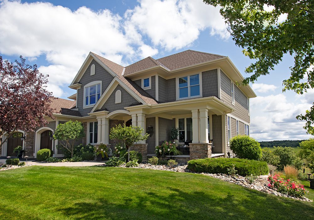Large house with a large lawn in front of it, surrounded by trees, plants, flowers, and stones