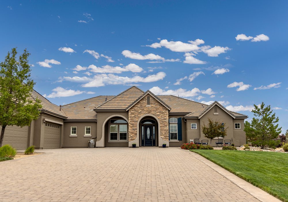 Large house with a driveway in front of it, surrounded by lush green grass, trees, and plants